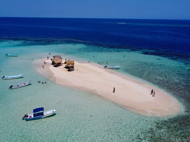 Luftaufnahme einer kleinen Sandbank-Insel mit strohgedeckten Hütten und Booten.