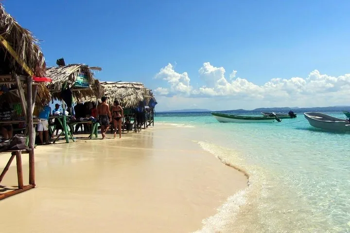 Touristen, die am Sandstrand nahe den Strohhütten von Cayo Arena entlanggehen.