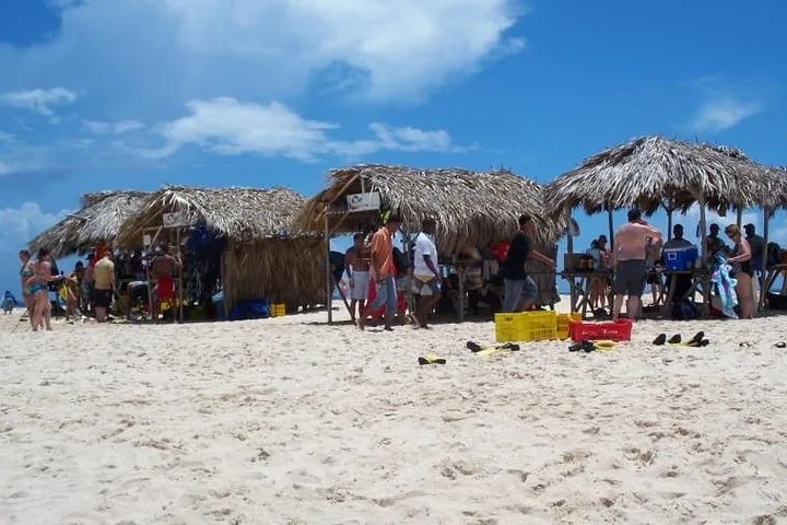 Mehrere Personen versammeln sich um Strohhütten am weißen Sandstrand von Cayo Arena.