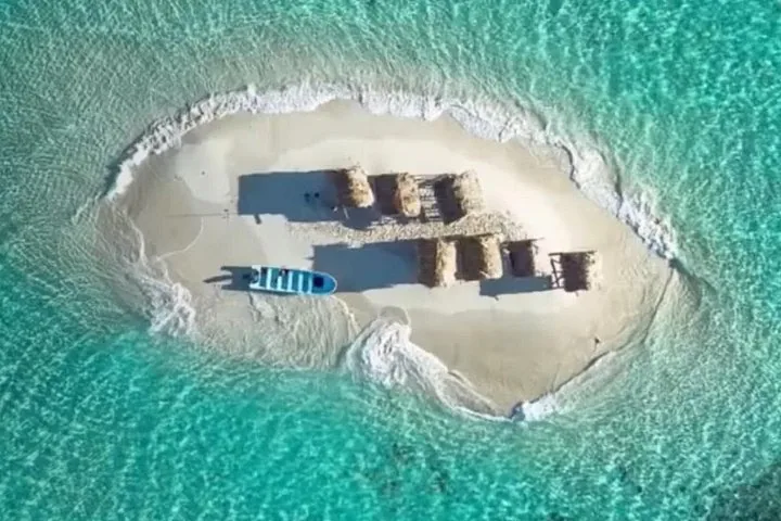 Luchtfoto van bovenaf van een klein zandeiland met hutten en een boot