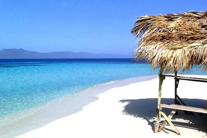 Ein Strohschirm an einem weißen Sandstrand mit Blick auf klares blaues Wasser